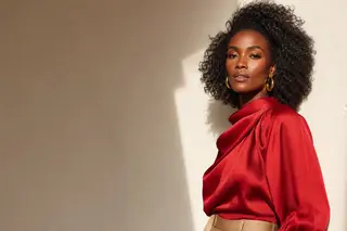 A confident woman in a sculptural cherry-red blouse and gold earrings